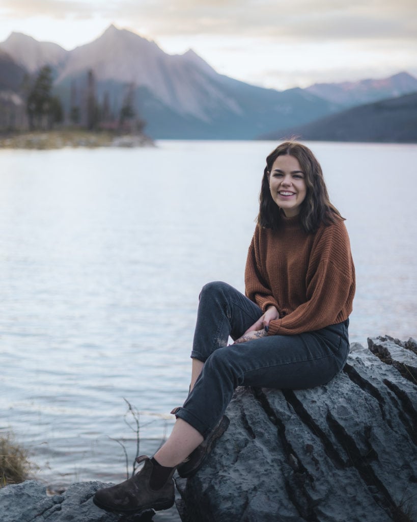 a girl sitting on a rock for a photo session during sunrise at medicine lake, jasper national park