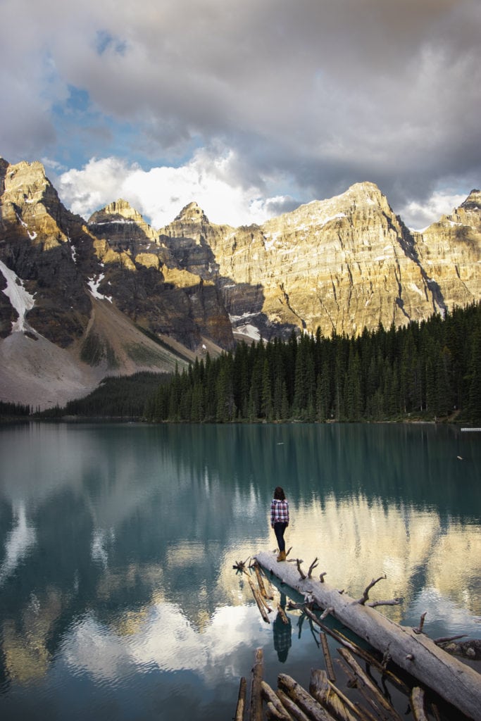 a photo of a girl walking out on a log at Moraine Lake, Banff National Park